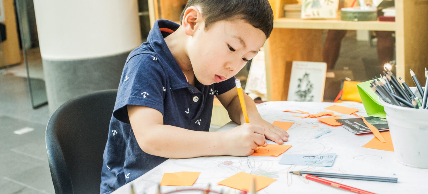 A small child colors on a piece of orange paper.
